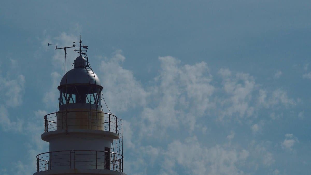 Cala Ratjada lighthouse in Spain with a clear blue sky and fluffy clouds.