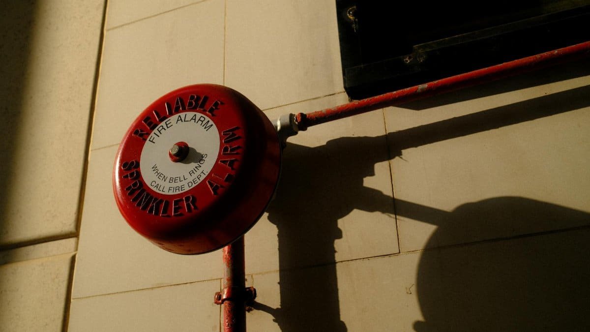 A red fire alarm bell with sprinkler system shadow on exterior wall in Hong Kong.