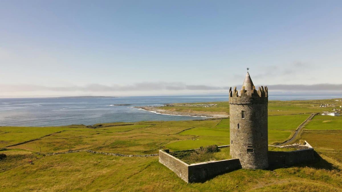Aerial view of Doonagore Castle in County Clare, Ireland with vibrant green fields and ocean.