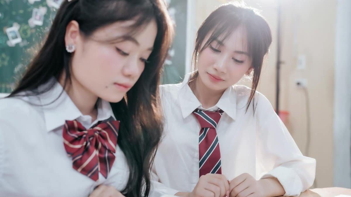 Two young women in school uniforms studying together in a bright classroom setting.