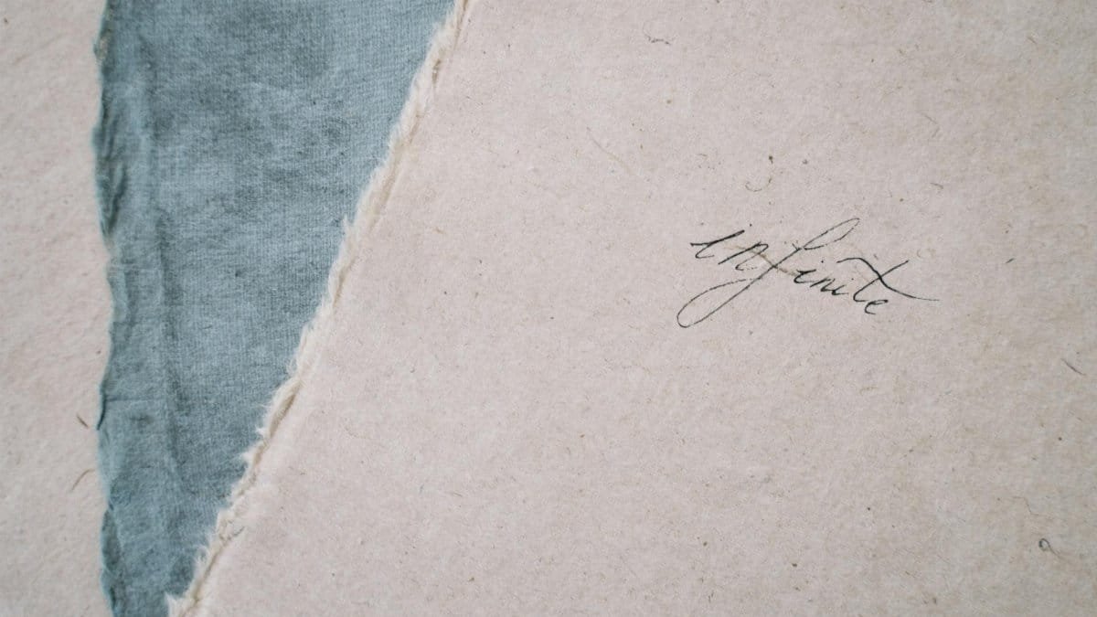Close-up of feathered fabric and paper with elegant handwritten 'infinite' text.