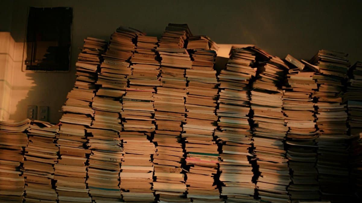 Piles of vintage books stacked against a dimly lit wall, suggesting history and knowledge.