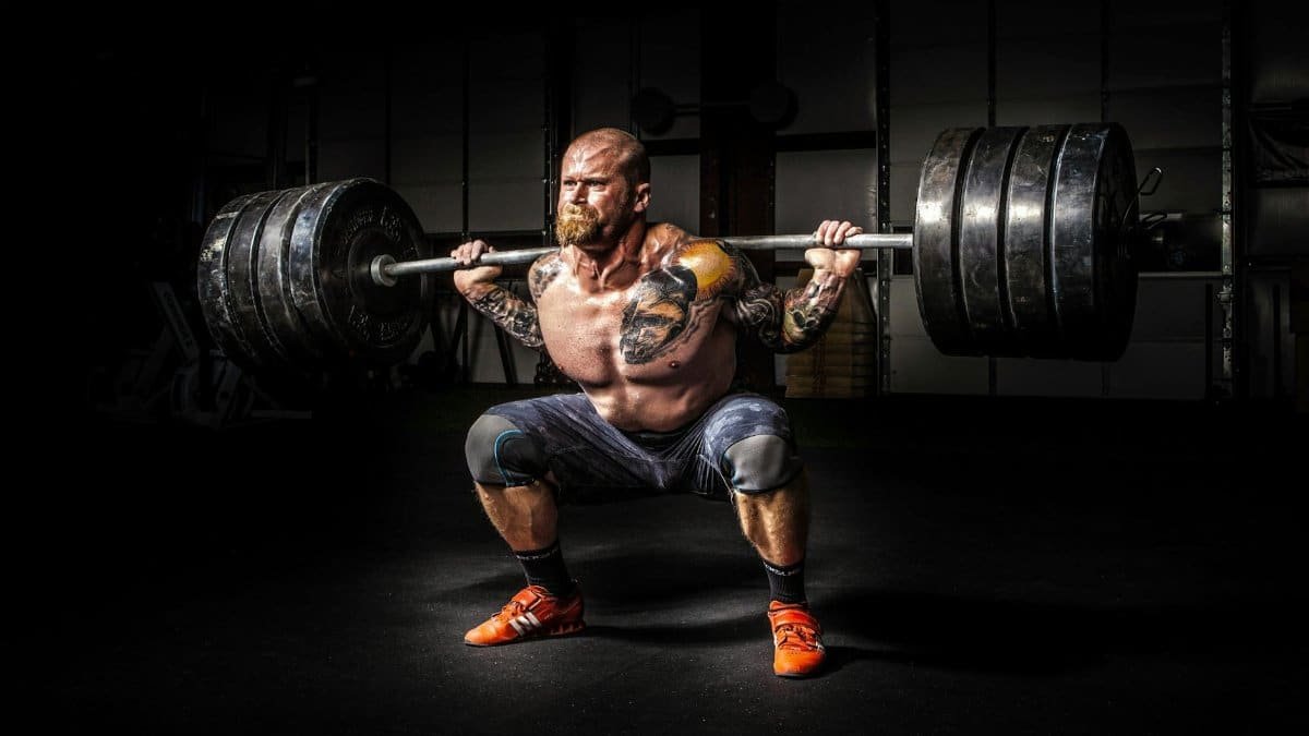 Muscular man lifting heavy weights during an intense squat session inside a gym.