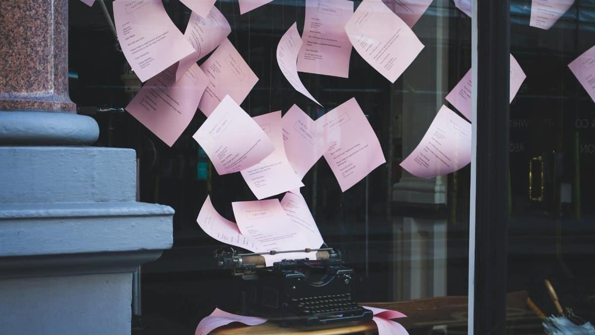 Artistic display of a vintage typewriter with pink papers floating in a window setting, indoors.
