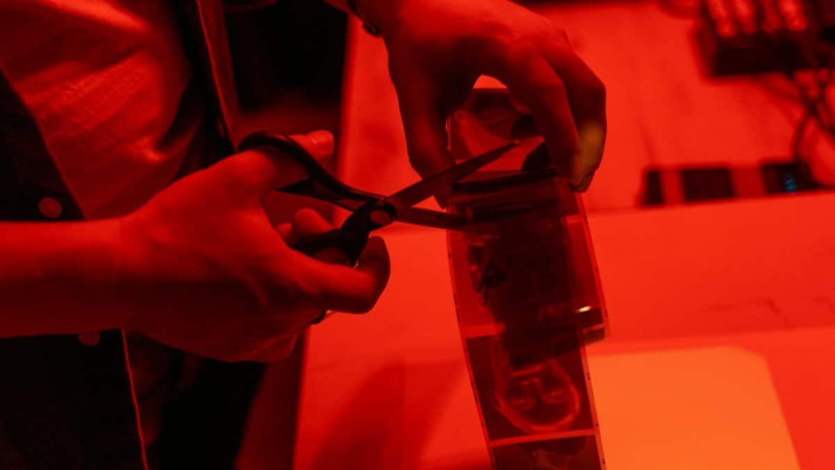 Close-up of a person cutting film negatives in a red-lit darkroom.