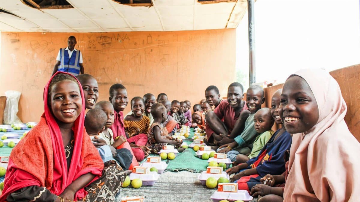 Group of cheerful African children sitting indoors sharing a meal, symbolizing togetherness and happiness.