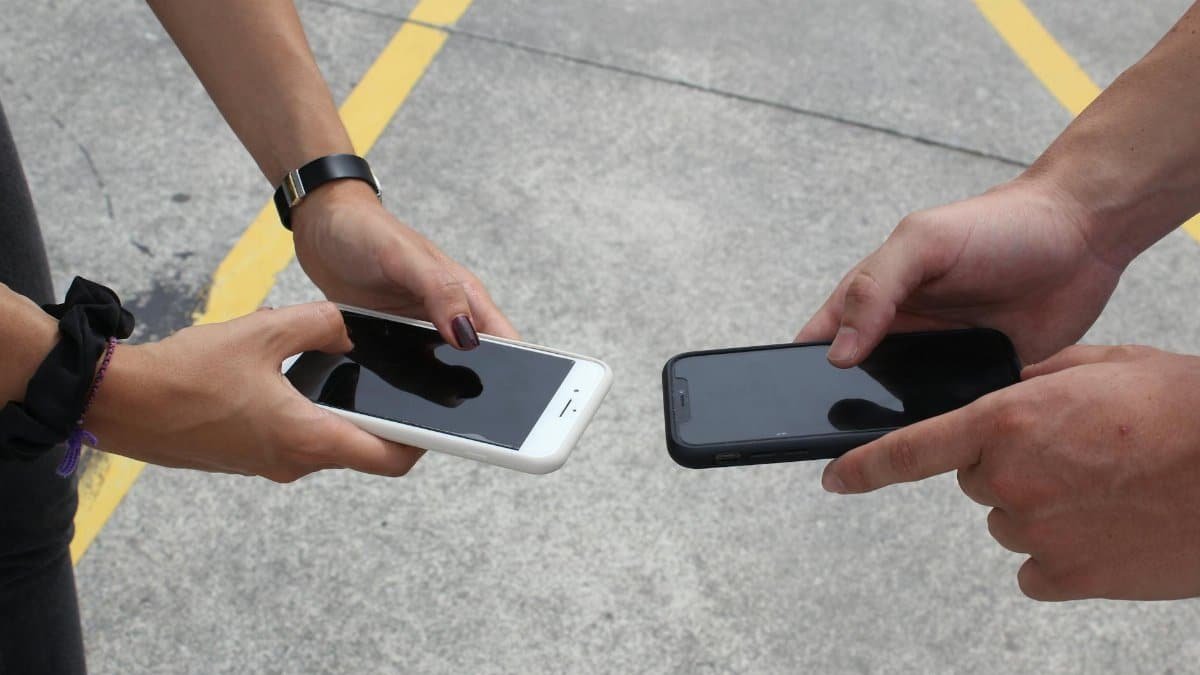 Two people exchanging or comparing smartphones in an outdoor setting, focusing on hands and technology.