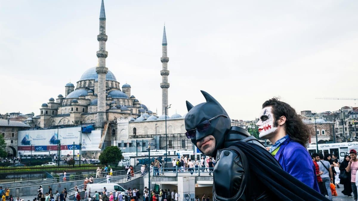 Cosplayers dressed as Batman and Joker in front of Istanbul's iconic Suleymaniye Mosque, a vibrant street scene.