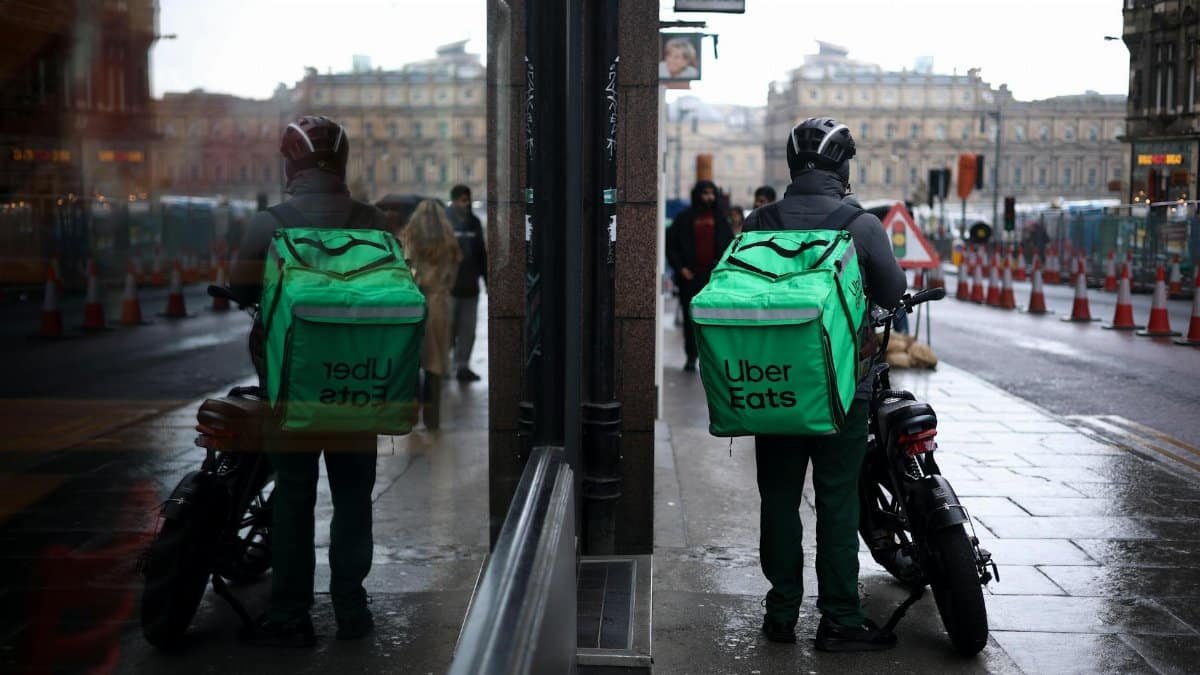Uber Eats courier on motorbike in Edinburgh with mirror reflection on rainy street day.
