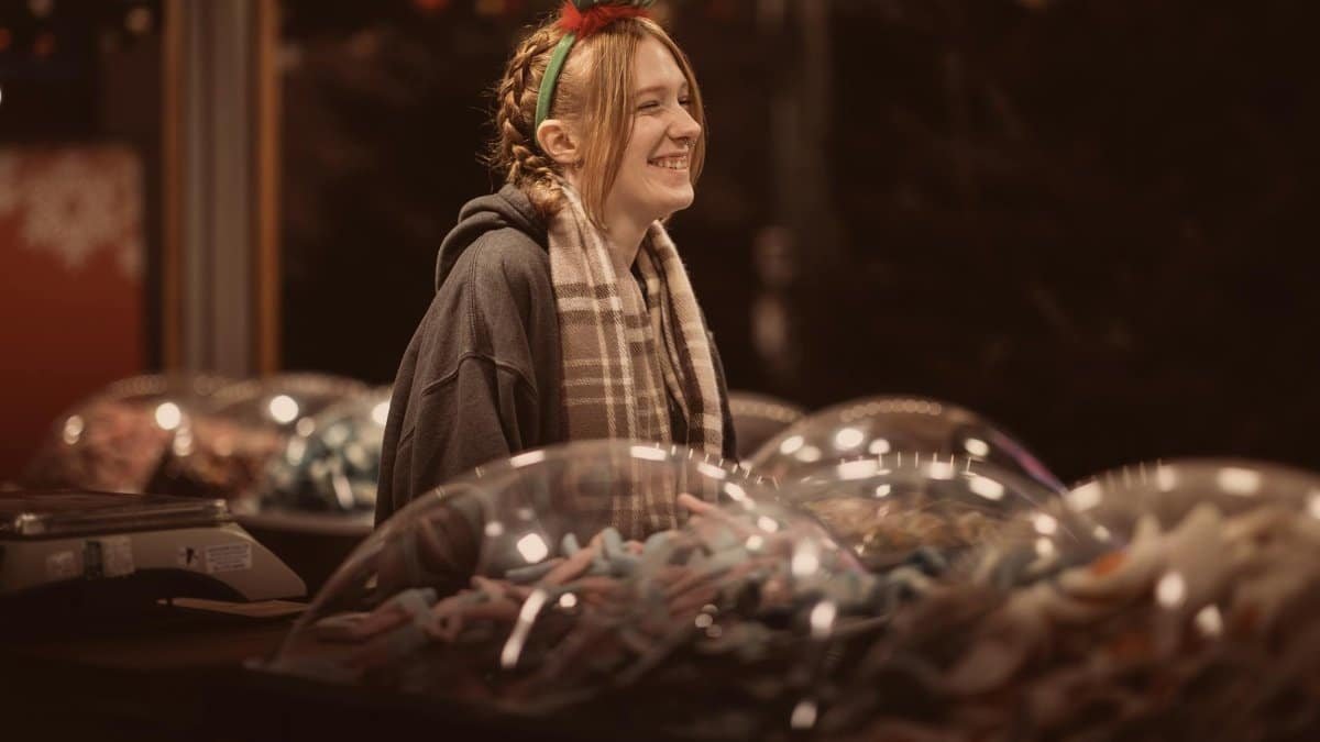 Vendor smiling at Bournemouth Christmas market, offering sweets in festive atmosphere.