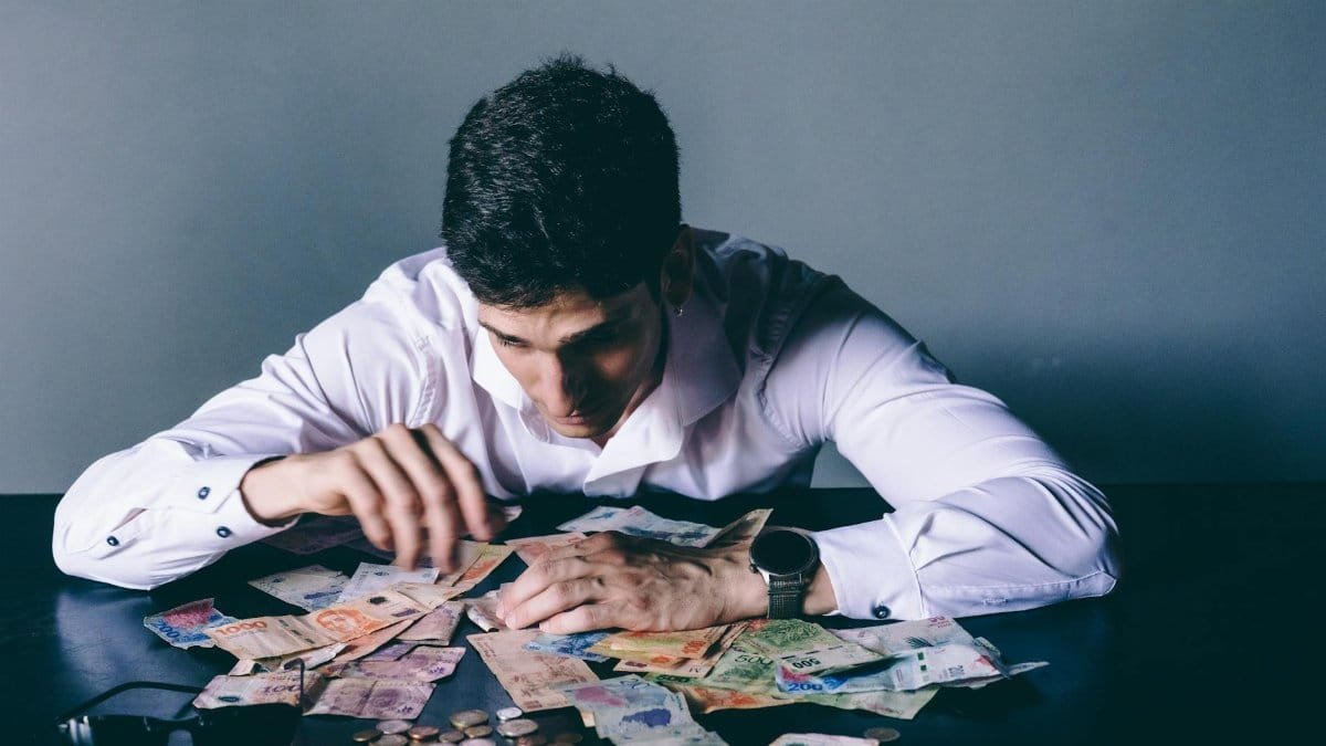 Focused man counts various international currencies on a dark desk indoors.
