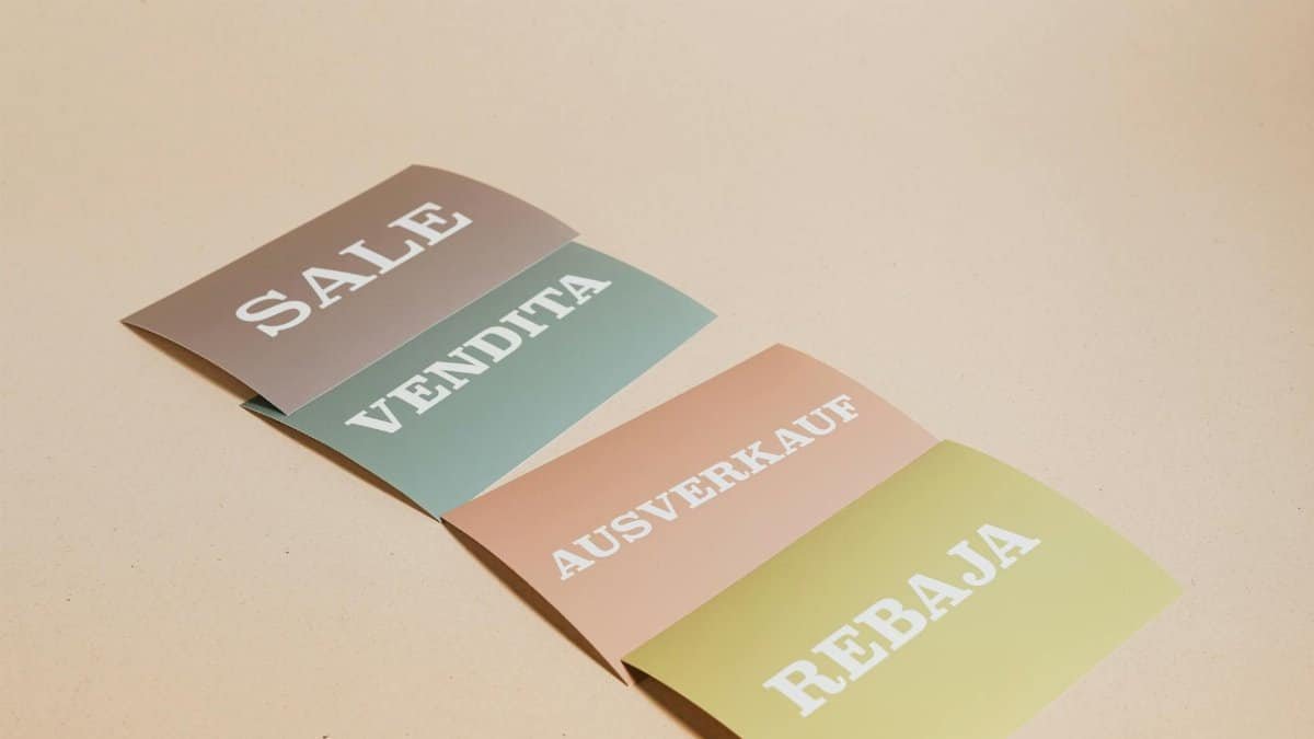 Four sale signs in different languages on a beige background, ideal for retail promotions.