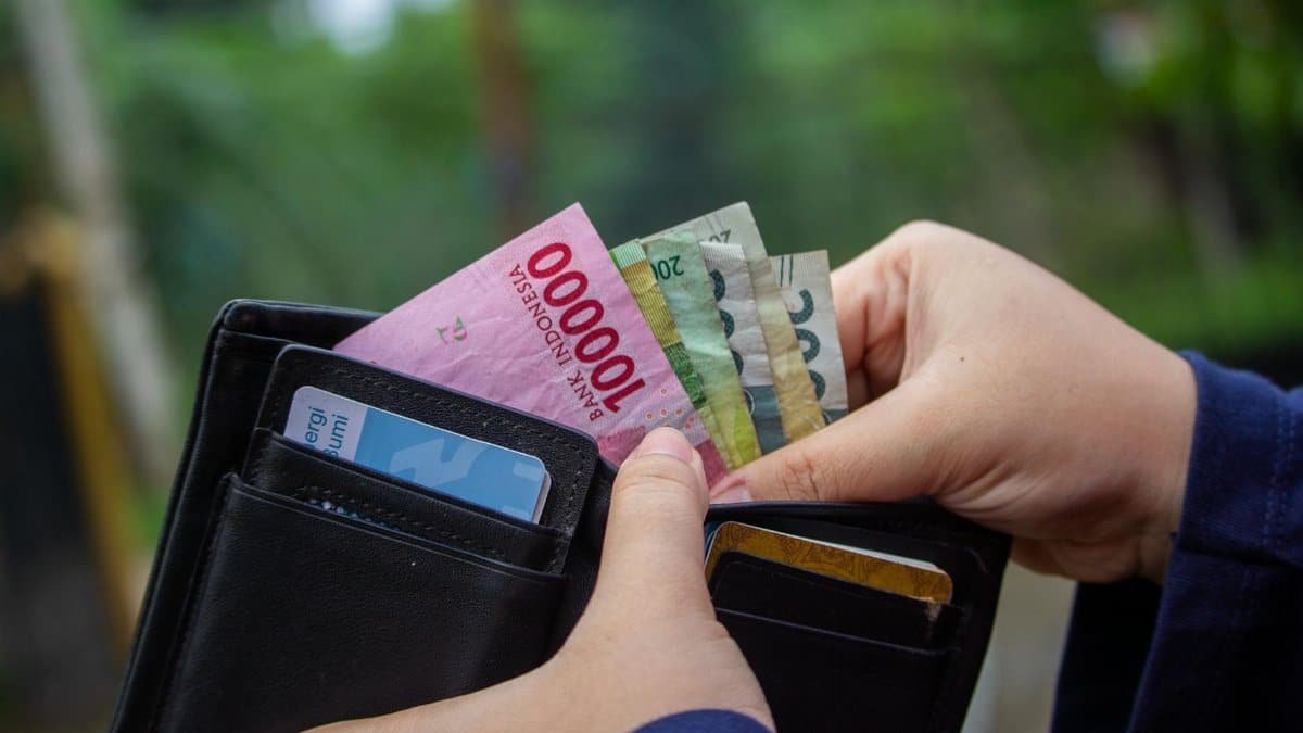Close-up of hands holding Indonesian rupiah notes in a wallet outdoors.