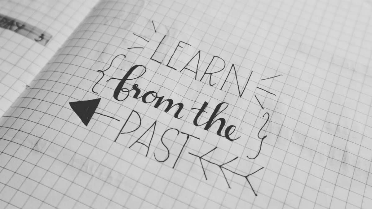 Black and white close-up of a handwritten motivational quote 'Learn from the Past' on graph notebook paper.