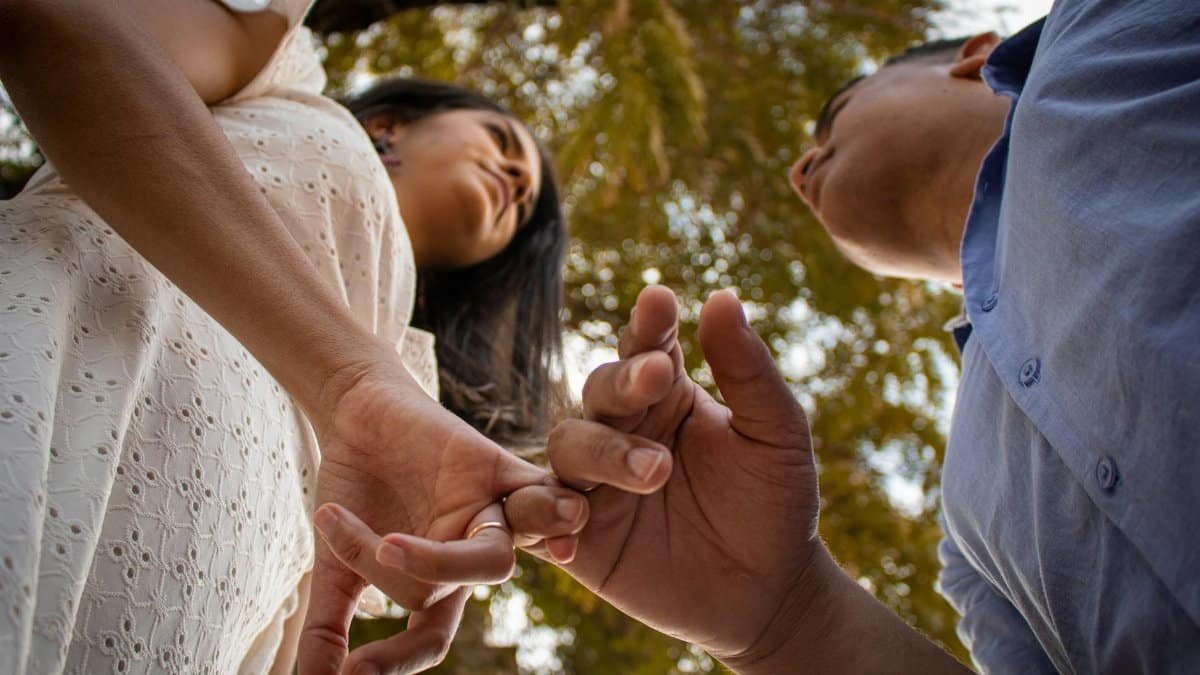 A couple making a pinky swear gesture while standing beneath a tree in Olinda, Brasil.