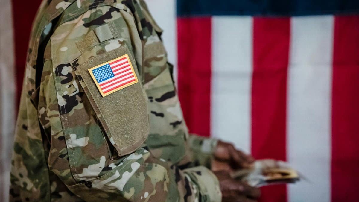 Close-up of a soldier in military uniform with American flag patch and background.
