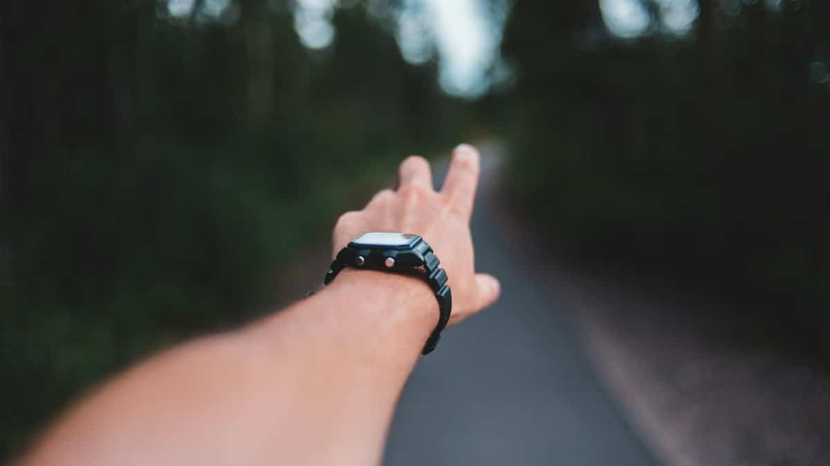 Blurred image of a man's hand reaching into a forest path wearing a wristwatch.