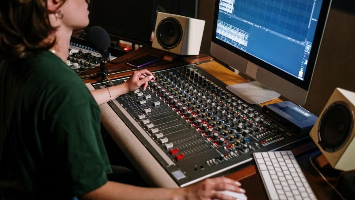 A sound engineer adjusting audio levels at a mixer desk in a recording studio with high-tech equipment.