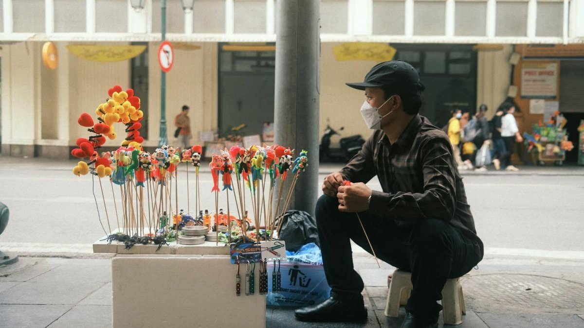 A street vendor with colorful toys sits on a busy urban sidewalk, showcasing lively city life.