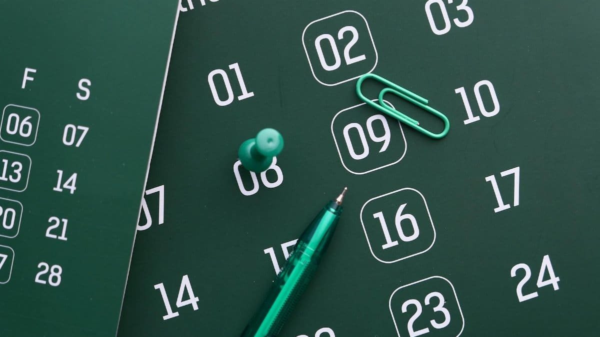 Close-up of a green calendar with pen, push pin, and paper clip for planning and organization.