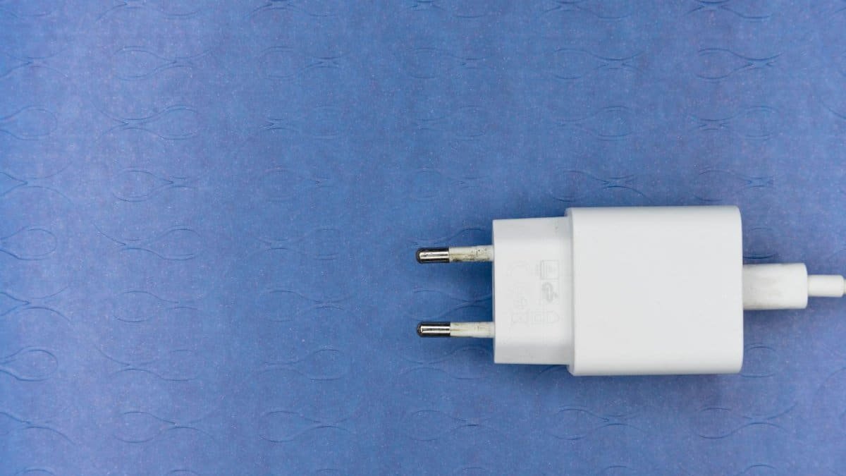 Close-up of a white electrical charger plug on a blue textured background, ideal for tech themes.