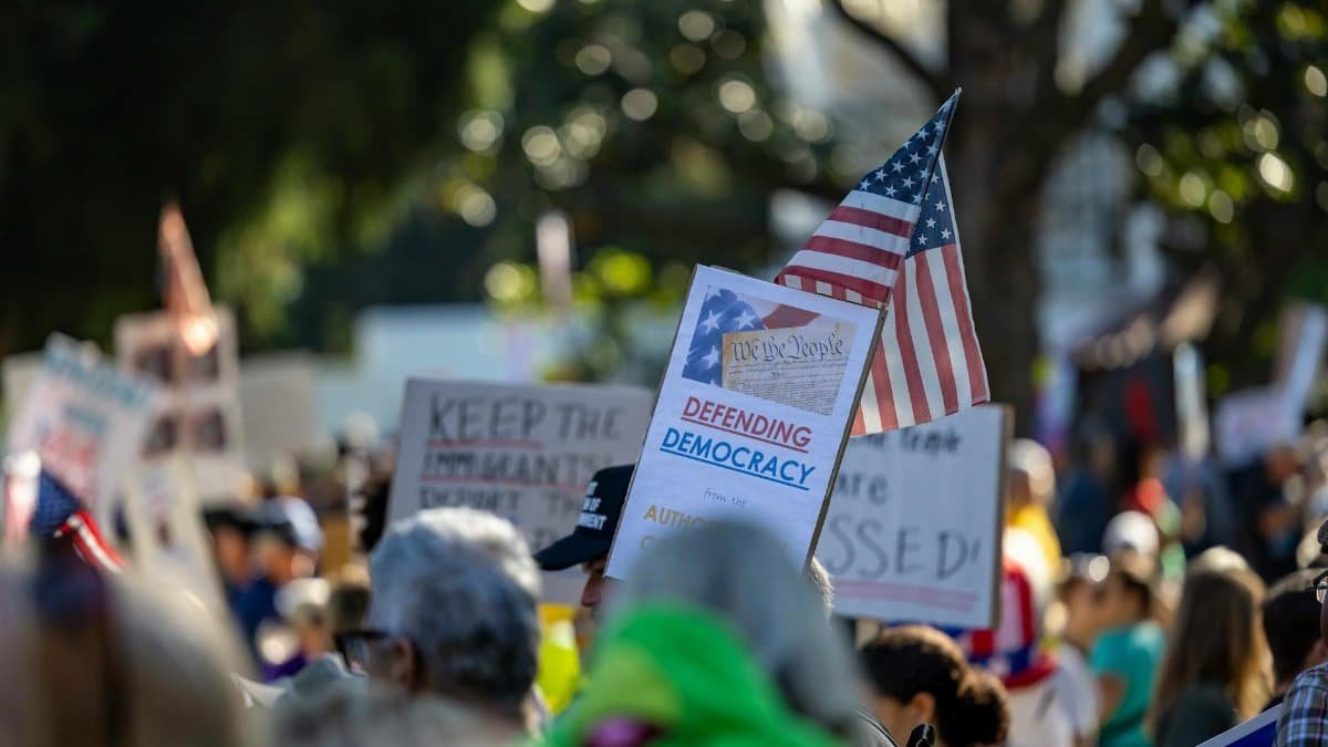 A crowd gathers in Sacramento, California to protest for defending democracy with signs and American flags.