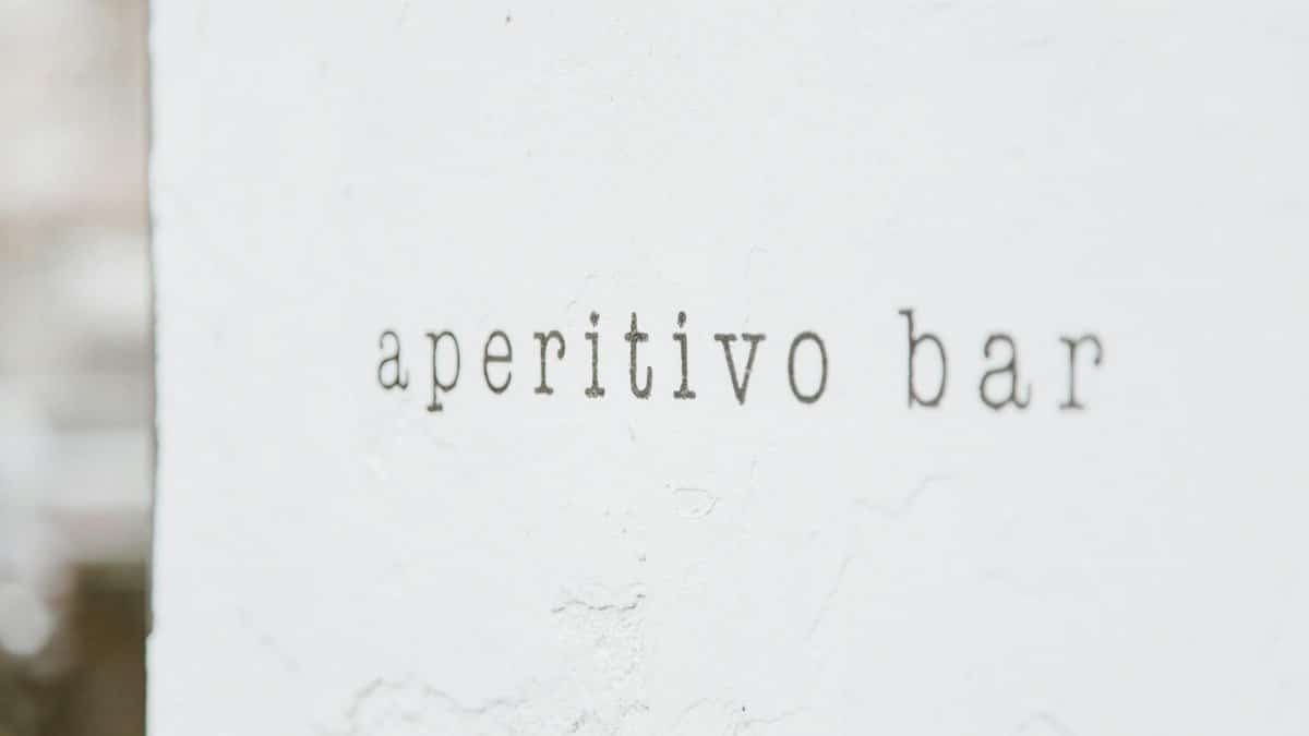 A minimalist image showing the text 'aperitivo bar' on a textured white wall, ideal for modern decor.