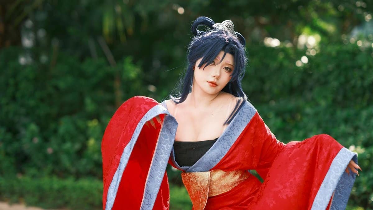 A cosplayer in a red kimono poses gracefully outdoors, showcasing detailed costume and vibrant colors.