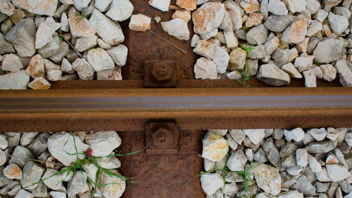 Rusty railway track close-up with gravel stones and greenery.