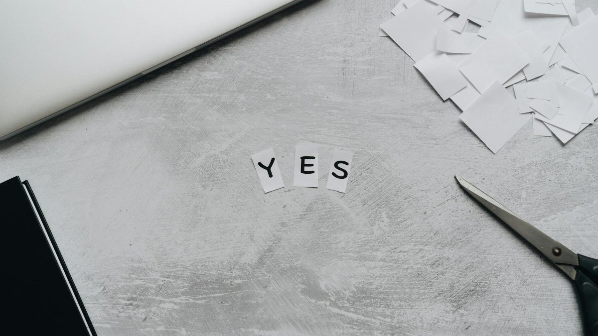 Artistic layout of paper cutouts forming 'YES' with scissors on a desk surface.