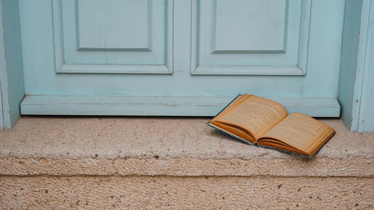 An open book rests on a rustic doorstep with a vintage blue door backdrop.