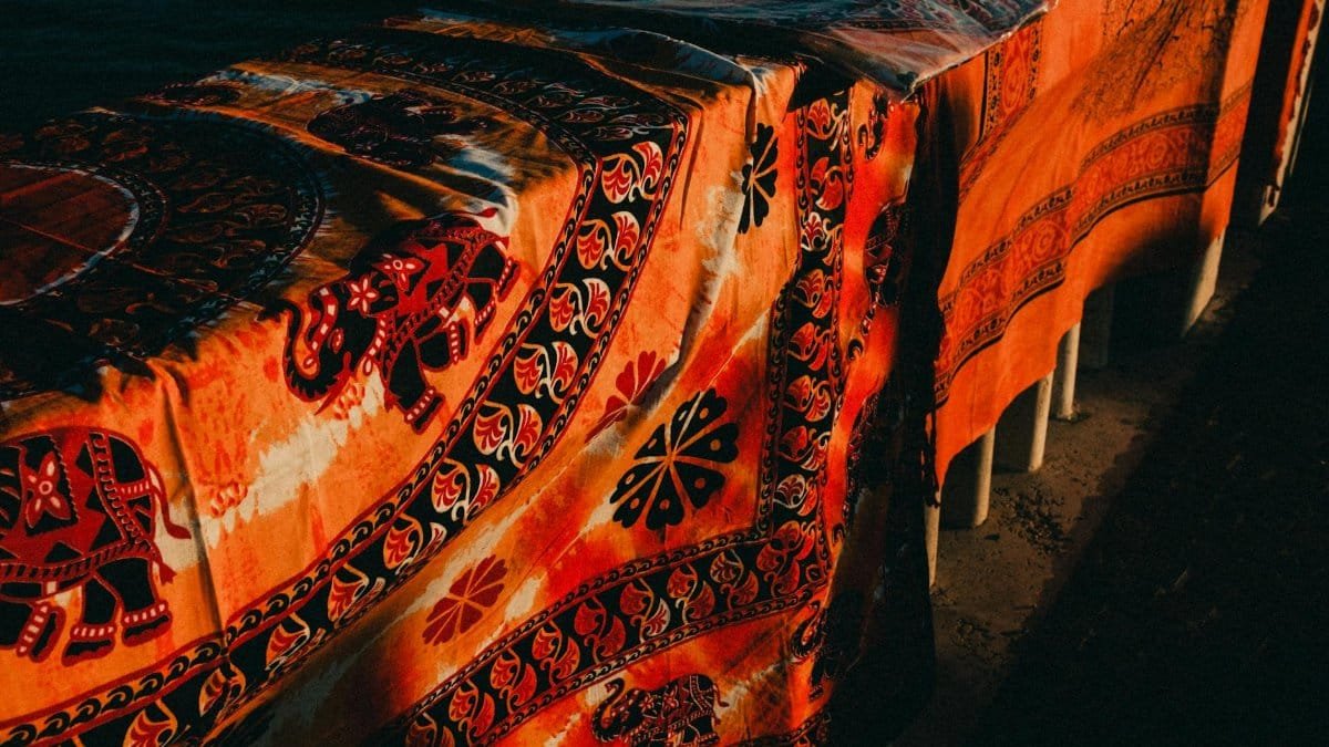 Richly colored fabric featuring elephants and ornate patterns draped outdoors with sunlight casting shadows.