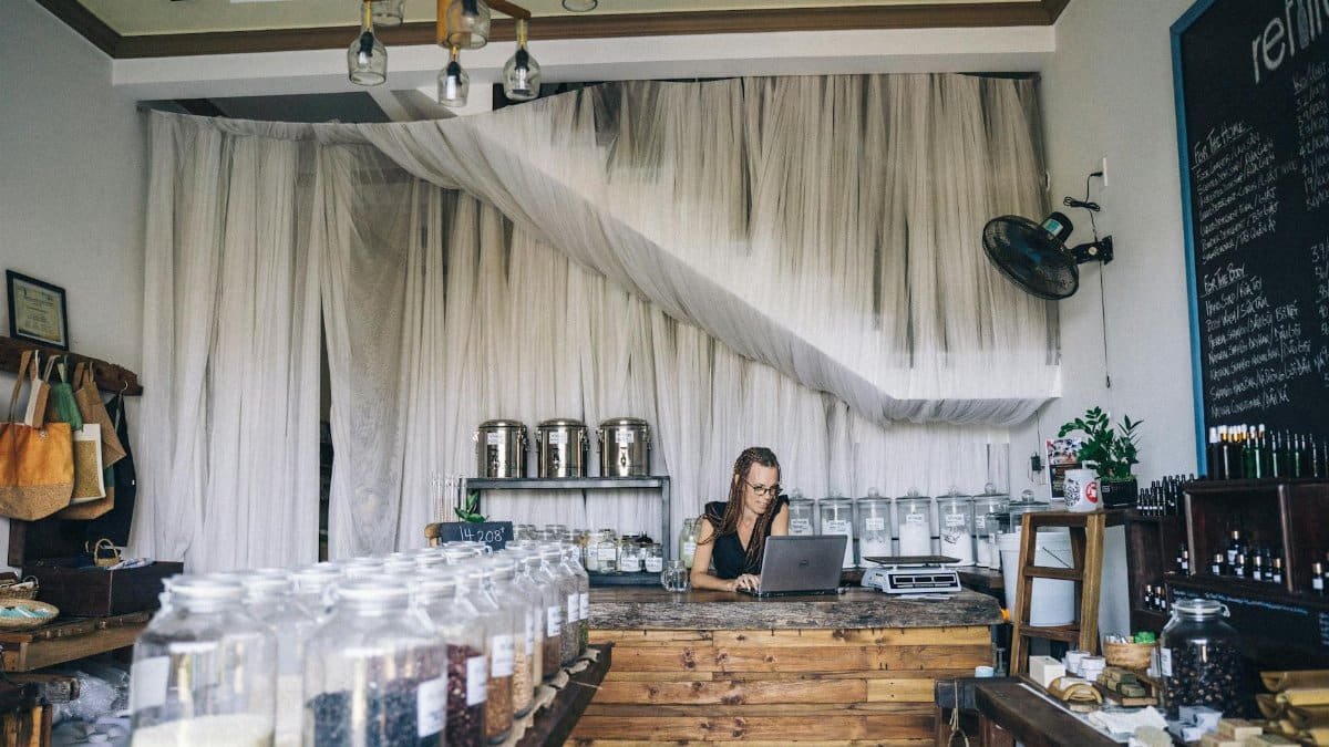 Woman working on laptop in eco-friendly store with glass jars and refillable items.