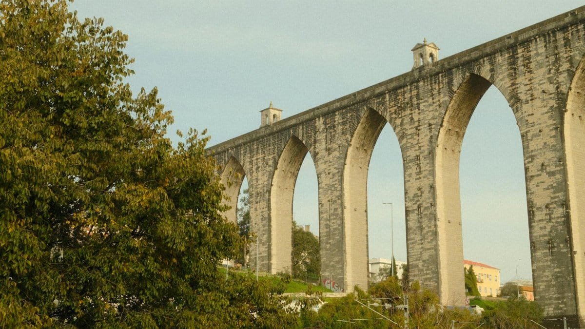 The majestic Águas Livres Aqueduct in Lisbon, Portugal, framed by lush greenery on a sunny day.