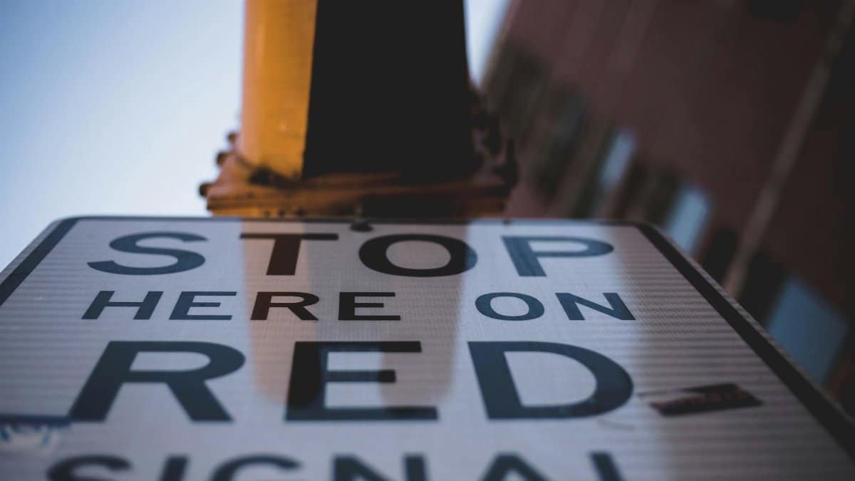 Low angle shot of a 'Stop Here on Red Signal' sign emphasizing urban traffic guidance.