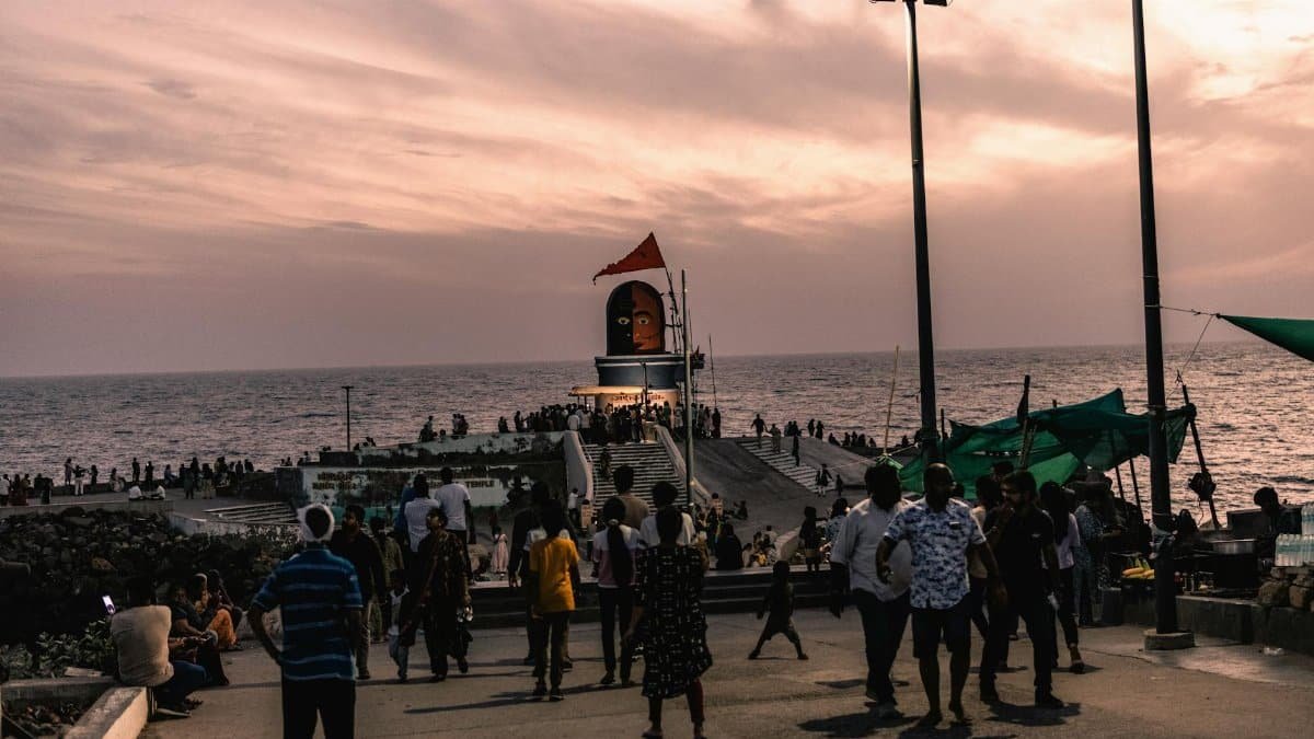 Crowds gather at sunset by the sea pier in Dwarka, India, under a colorful sky.