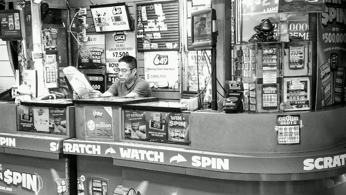 A man reads at a busy lottery ticket booth filled with signs and advertisements.