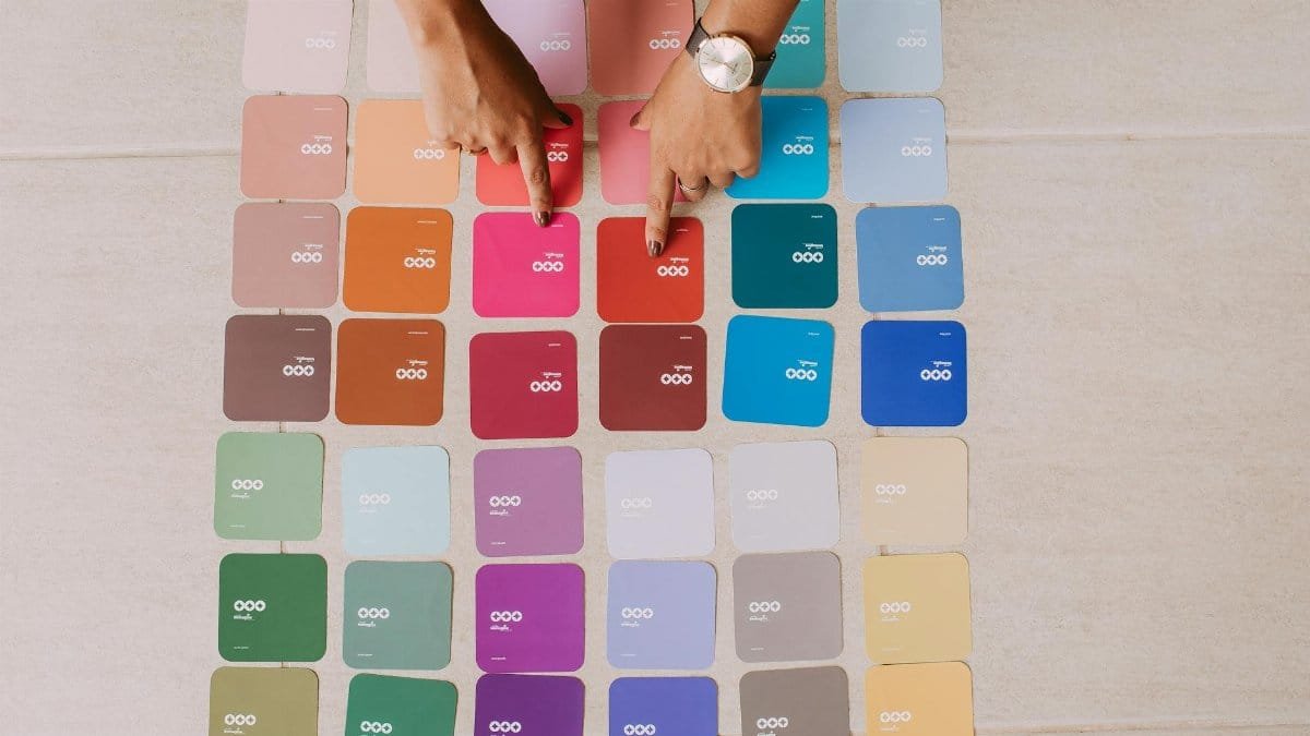 Top view of hands pointing at various color palette cards on a table, showcasing diverse options.
