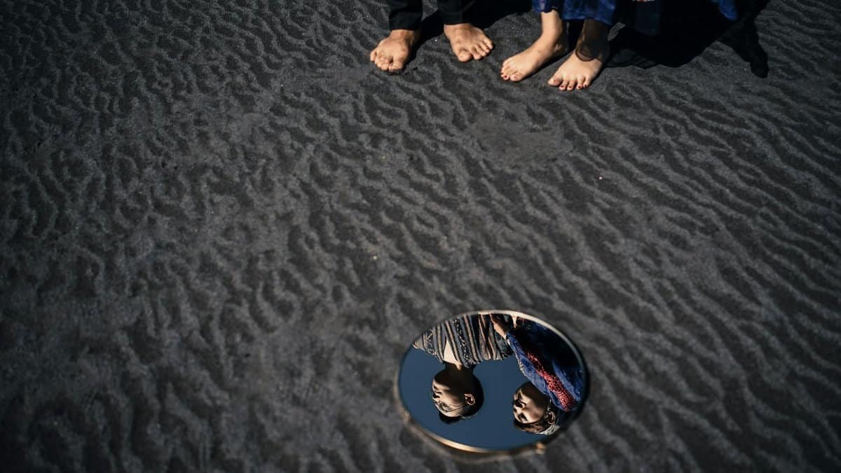 A creative photo of a couple's reflection in a mirror placed on sand, showcasing artistic elegance.