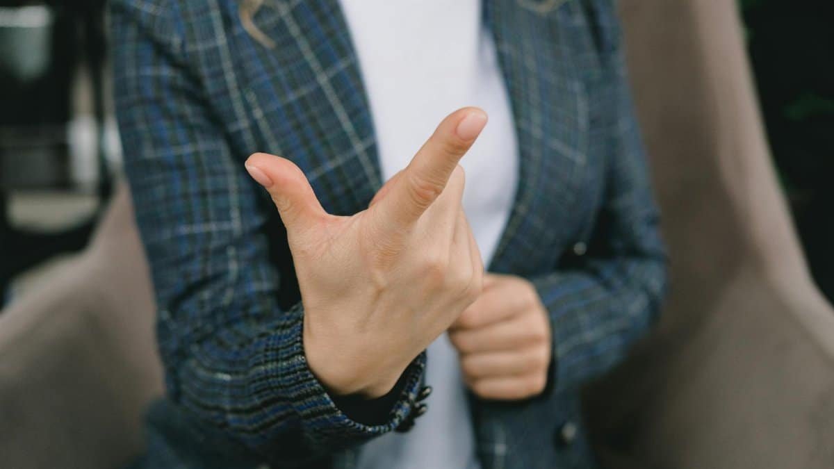 Crop anonymous lady in elegant blazers sitting in comfortable armchair and showing index finger while communicating using sign language