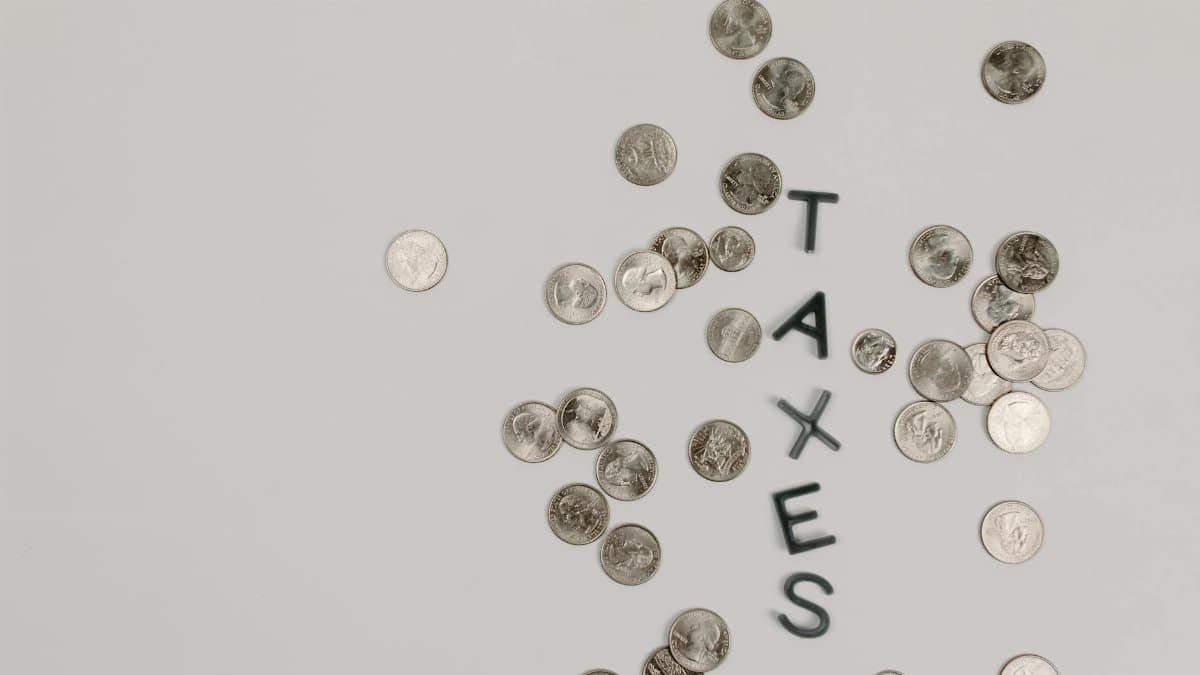 Scattered coins forming the word 'TAXES' on a white surface, symbolizing financial concepts.