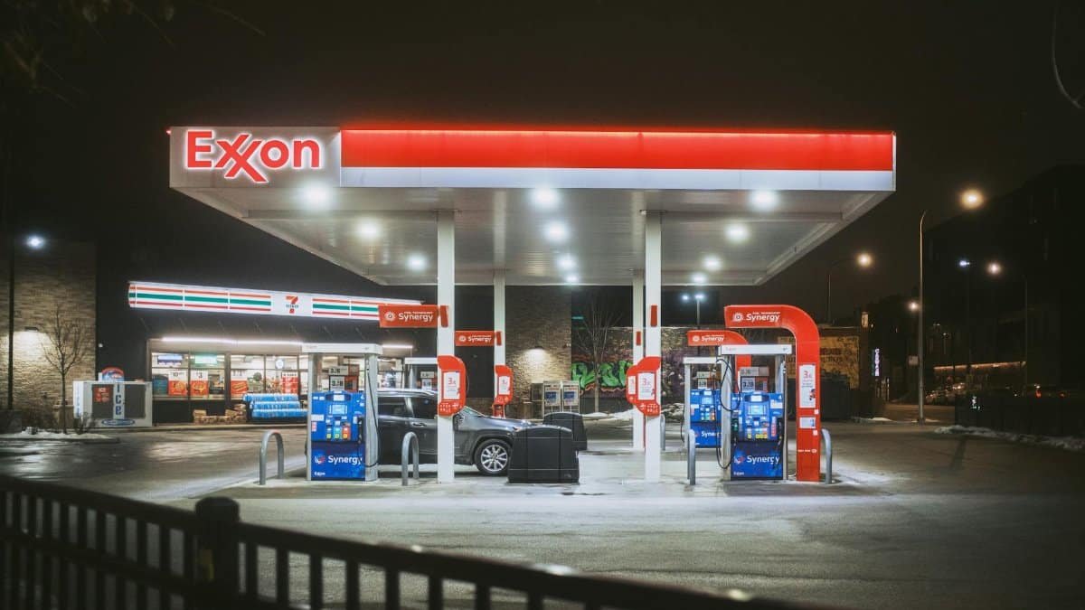 A brightly lit Exxon gas station and 7-Eleven store at night, featuring fuel pumps and a parked car.