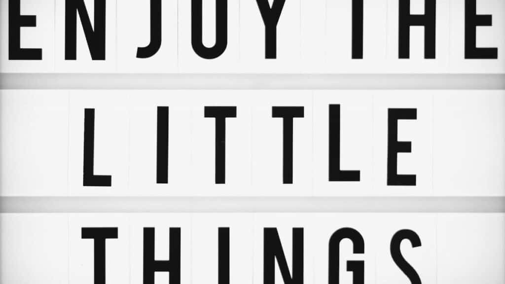 Minimalist design of the inspirational quote 'Enjoy The Little Things' displayed on a lightbox.