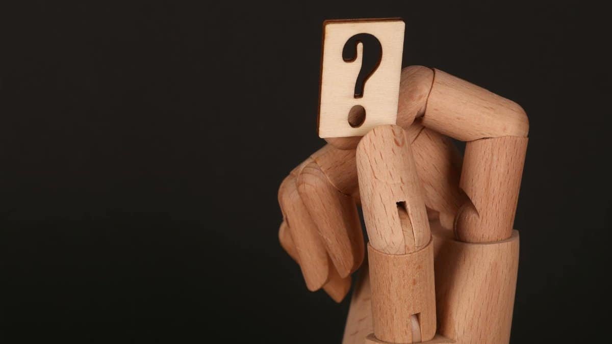 Close-up of a wooden mannequin hand holding a block with a question mark, emphasizing curiosity.
