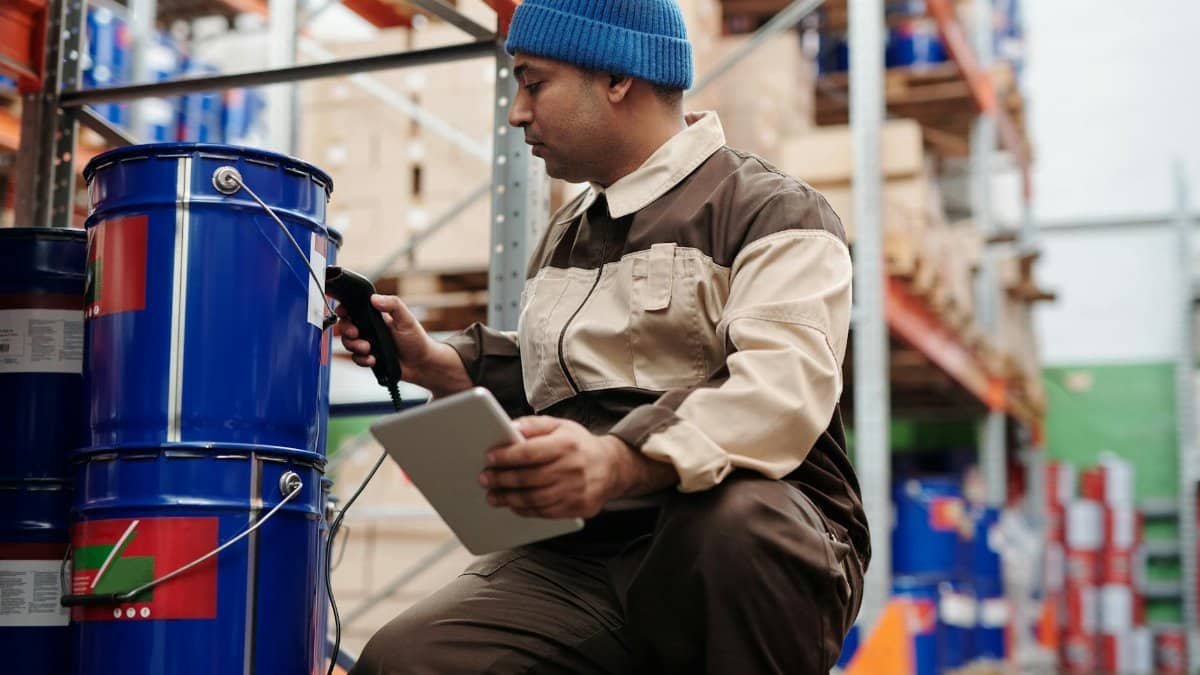 Warehouse employee scanning inventory using tablet and scanner in industrial storage area.