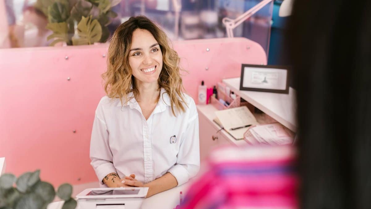 Smiling receptionist at a salon front desk, welcoming clients with a friendly demeanor.