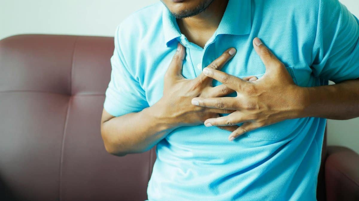 A close-up image of a man clutching his chest, indicating heart pain or discomfort.