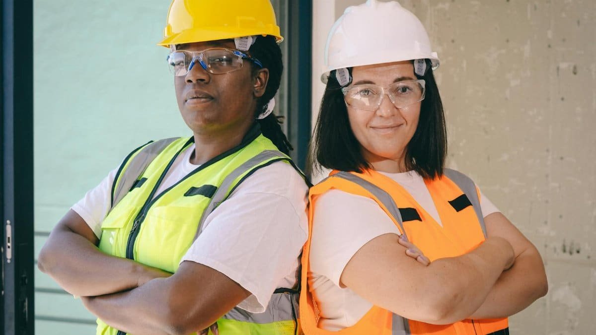 Two female engineers wearing safety gear stand confidently with crossed arms indoors.
