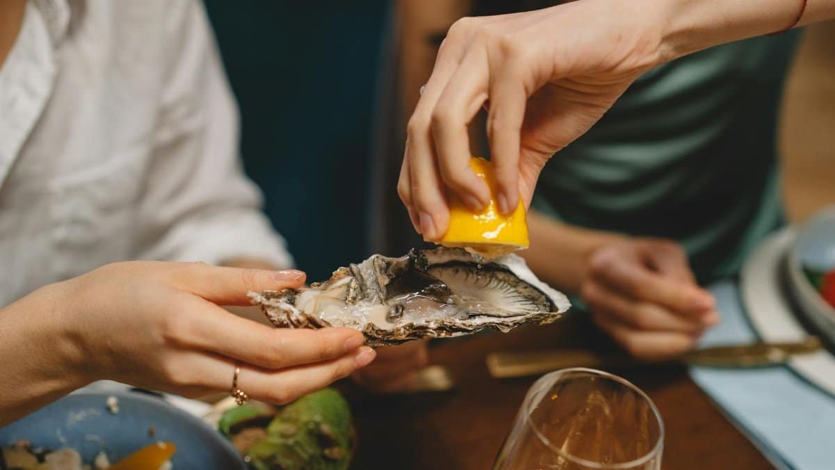 Hands preparing a fresh oyster with a lemon squeeze at a dinner setting. Perfect for seafood lovers.