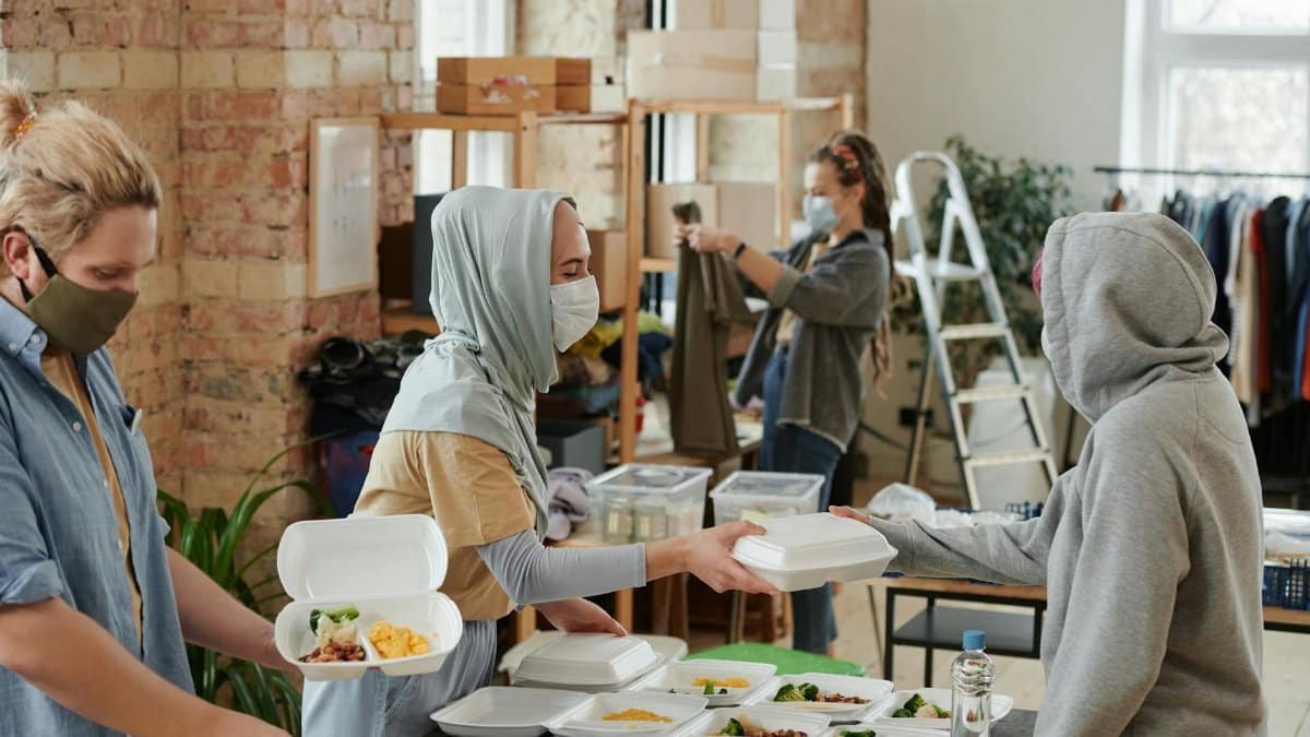 Volunteers wearing face masks distribute food in takeaway boxes at a community charity event.